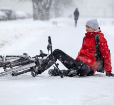 Fallen down Caucasian cyclist sitting on slippery roadside, riding bicycle in city at winter season